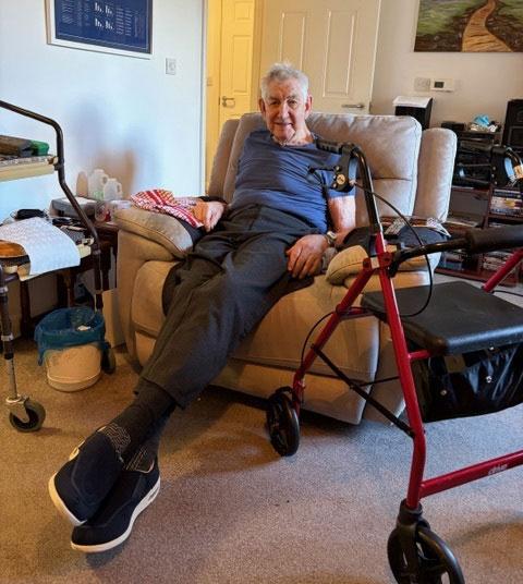 man sitting in arm chair at home with walking aid to the side